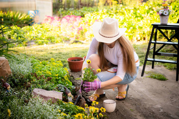 Bahçeyle uğraşan genç bir kadın, saksıya çiçek ekiyor. - Fotoğraf, Görsel