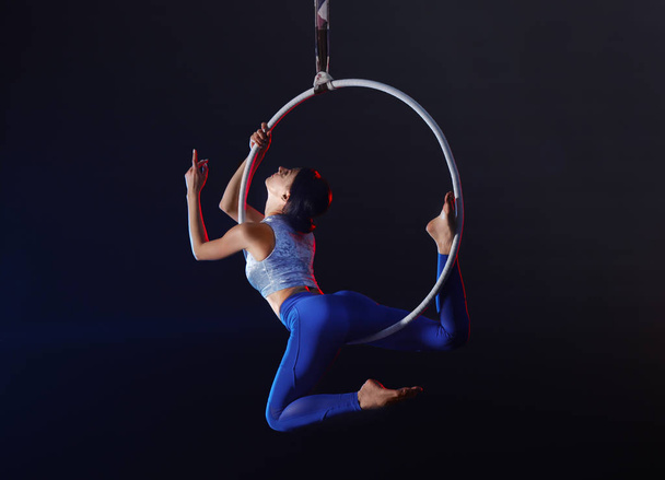 Young woman performing acrobatic element on aerial ring indoors - Fotografie, Obrázek