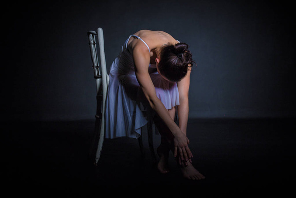 dancer sitting on chair in studio in forward bend - Фото, изображение