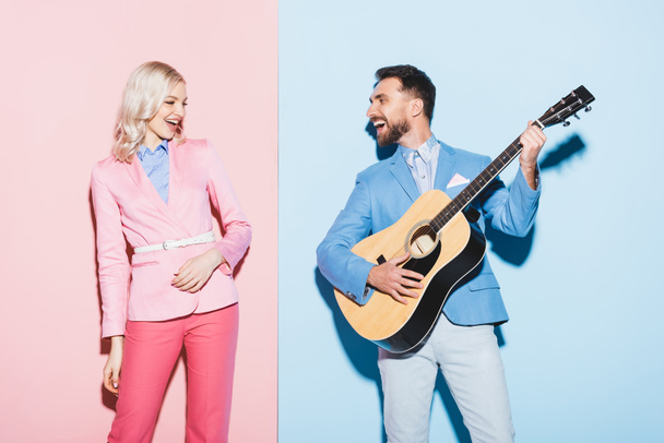 smiling woman and handsome man playing acoustic guitar on pink and blue background  - Foto, imagen