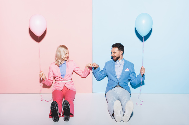 Lächelnde Frau und gutaussehender Mann mit Luftballons, die Faust in Faust Geste auf rosa und blauem Hintergrund zeigen  - Foto, Bild