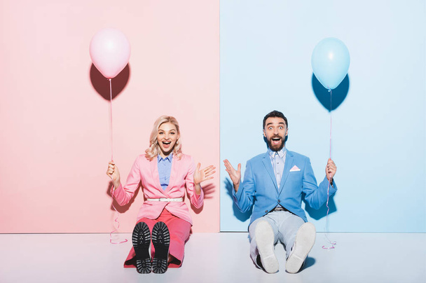 wstrząśnięty kobieta i przystojny mężczyzna trzymając balony na różowym i niebieskim tle  - Zdjęcie, obraz