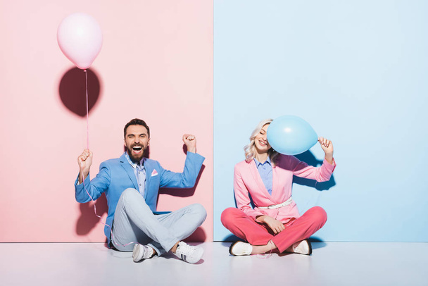 attractive woman and handsome man with balloons showing yes gesture on pink and blue background  - Fotó, kép
