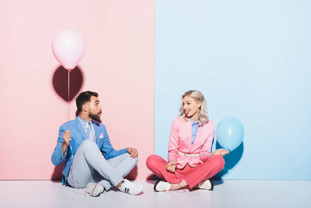 attractive woman sticking out tongue and looking at man with balloon on pink and blue background  - 写真・画像