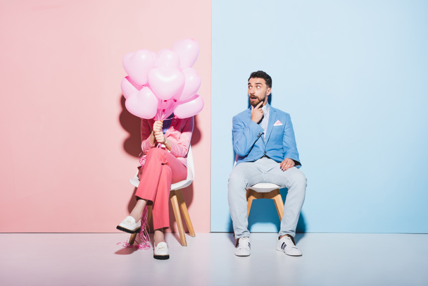 woman holding balloons and shocked man on pink and blue background  - Foto, immagini