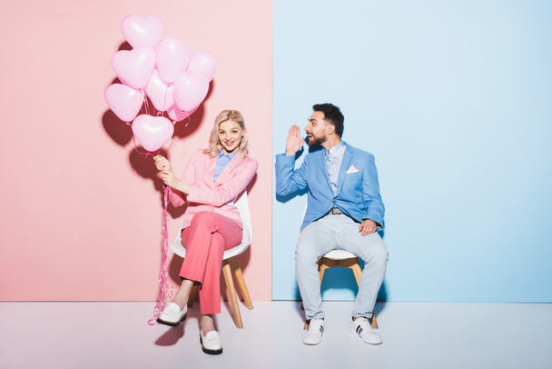 smiling woman holding balloons and handsome man on pink and blue background  - 写真・画像