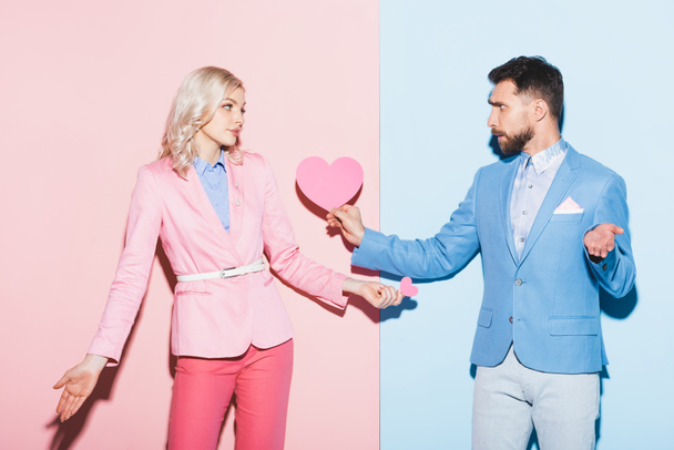 sad woman and handsome man holding heart-shaped cards on pink and blue background  - Фото, изображение