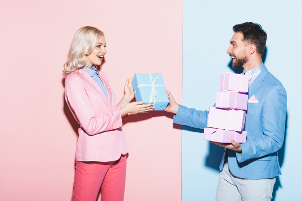 knappe man geven geschenk aan glimlachende vrouw op roze en blauwe achtergrond  - Foto, afbeelding