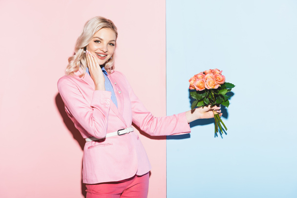 smiling woman holding bouquet on pink and blue background - Photo, image