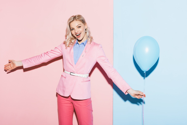 smiling woman holding balloon on pink and blue background  - Foto, afbeelding