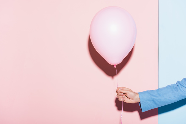 περικοπή άποψη του ανθρώπου κρατώντας μπαλόνι σε μπλε και ροζ φόντο  - Φωτογραφία, εικόνα
