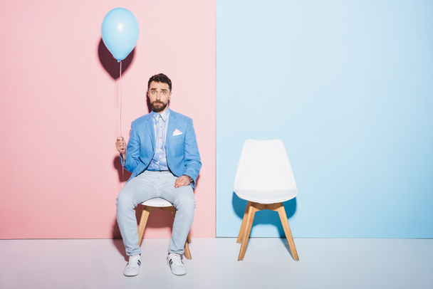 handsome and sad man holding balloon on blue and pink background  - Fotoğraf, Görsel