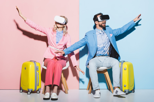 woman and smiling man in virtual reality headsets with outstretched hands on pink and blue background  - Foto, afbeelding