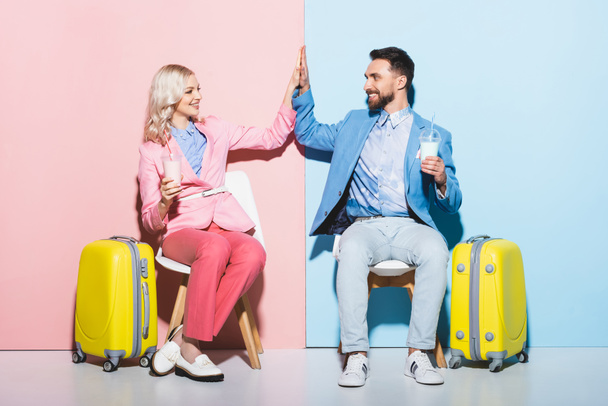smiling woman and handsome man showing high five and holding cocktails on pink and blue background  - Фото, зображення
