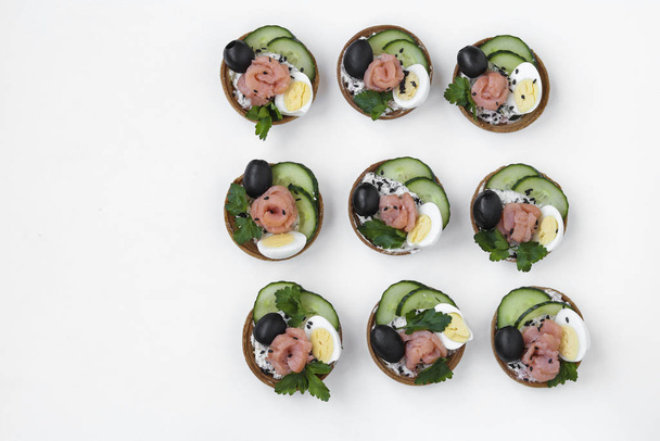 Holiday tartlets with cheese, salmon, black olives, quail eggs and cucumbers on white background, Top view, Copy space - Foto, immagini