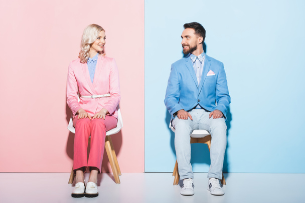 χαμογελαστή γυναίκα και όμορφος άντρας κοιτάζονται σε ροζ και μπλε φόντο  - Φωτογραφία, εικόνα