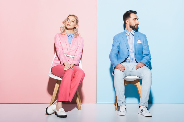 dreamy woman and handsome man sitting on chairs on pink and blue background  - Foto, afbeelding