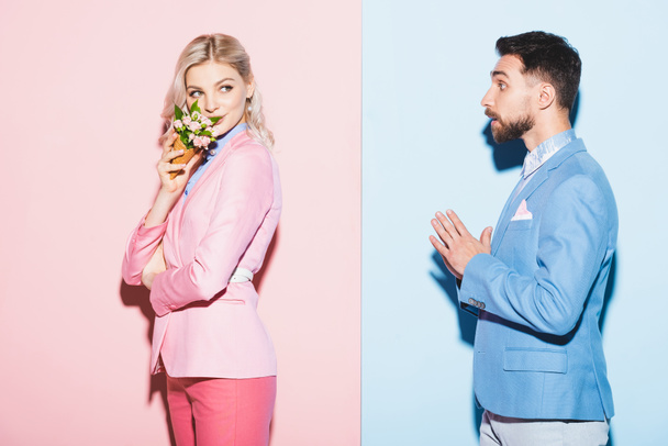 donna attraente che tiene bouquet e bell'uomo che la guarda su sfondo rosa e blu
  - Foto, immagini