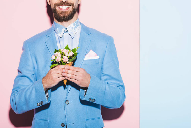 cropped view of smiling man holding bouquet on pink and blue background  - Photo, Image