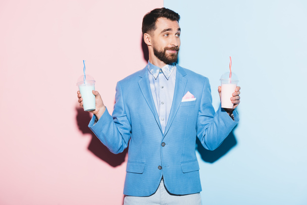 Lächelnder Mann mit Cocktails auf rosa und blauem Hintergrund  - Foto, Bild