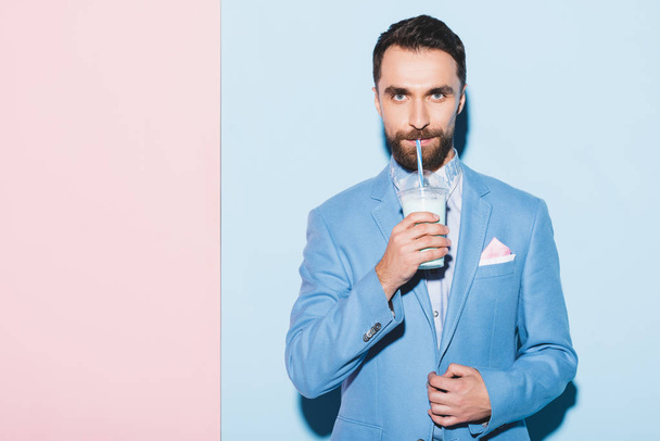 handsome man drinking cocktail on pink and blue background  - Фото, зображення