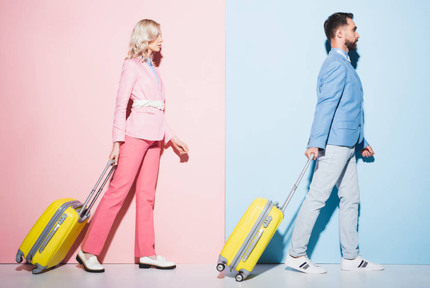 oldalnézetben vonzó nő és jóképű férfi séta utazási táskák rózsaszín és kék háttér  - Fotó, kép