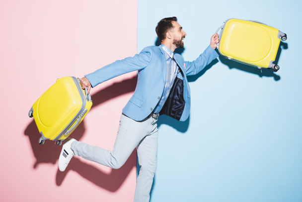 mosolygós férfi gazdaság utazási táskák rózsaszín és kék háttér  - Fotó, kép