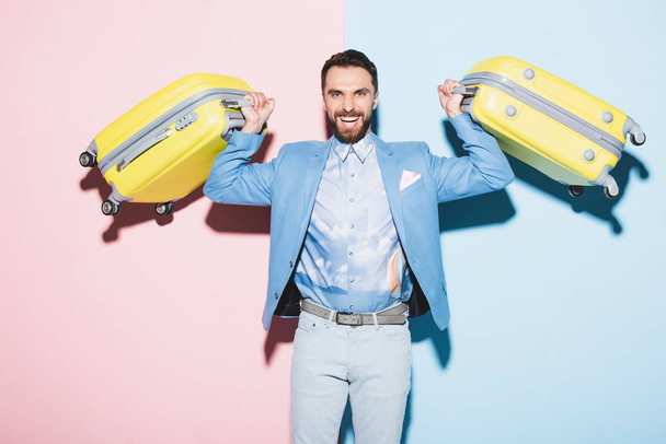 smiling man holding travel bags on pink and blue background  - Foto, imagen