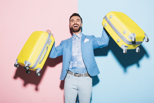 Gülümseyen adam pembe ve mavi arka planda seyahat çantaları taşıyor.  - Fotoğraf, Görsel