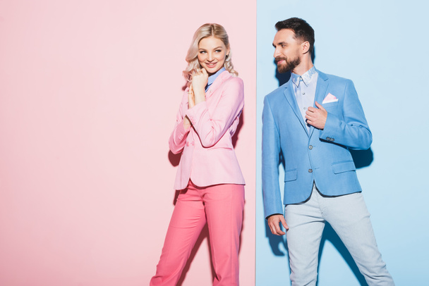 attraktive Frau und lächelnder Mann, der sie auf rosa und blauem Hintergrund ansieht  - Foto, Bild