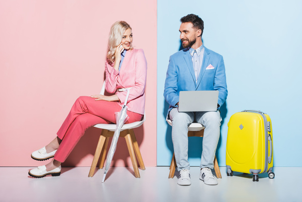 mosolygós nő beszél okostelefon és jóképű férfi laptop rózsaszín és kék háttér  - Fotó, kép