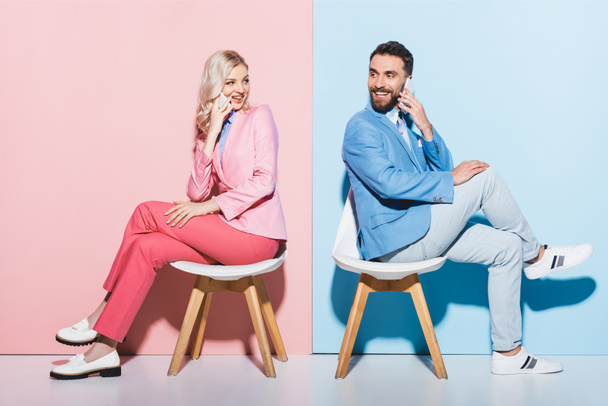 smiling woman and handsome man talking on smartphones on pink and blue background  - Fotó, kép