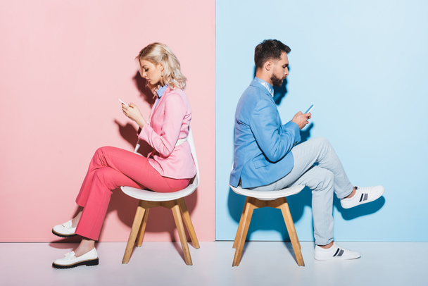 side view of woman and handsome man using smartphones on pink and blue background  - Foto, imagen