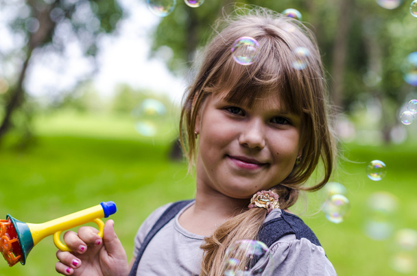 Little girl playing with soap bubbles in summer park - Foto, afbeelding