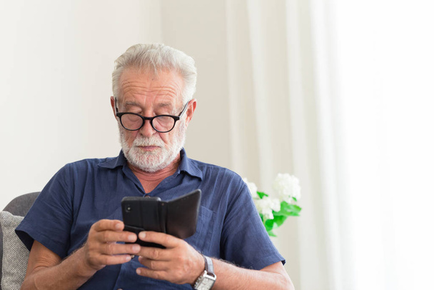 старша сіра борода біле волосся в окулярах, дивлячись уваги на його смартфон, щоб читати новини вдома поодинці
. - Фото, зображення
