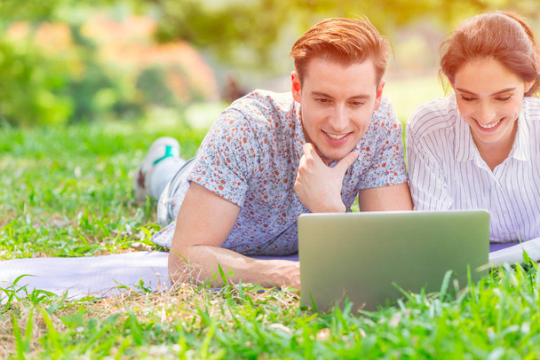 Çift iş aşığı yan yana dizüstü bilgisayara bakıp mutlu ve açık yeşil parka gülümsüyor.. - Fotoğraf, Görsel