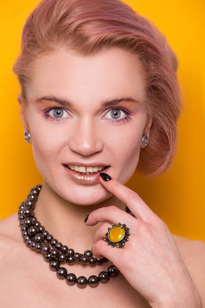 Shiny golden make-up on a beautiful young European model girl isolated on an orange background in the photo studio - Foto, imagen