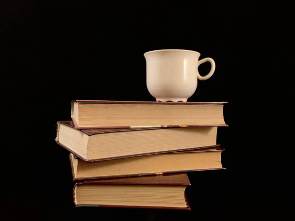 Libros cerrados y una taza de café sobre un fondo negro. Una taza de té y un libro de tapa dura
. - Foto, Imagen
