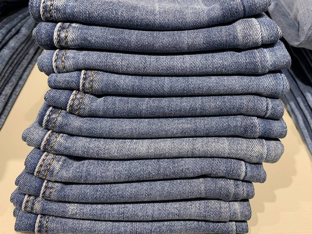 Stapels moderne jeans van verschillende maten. Een selectie van jeans in een kledingwinkel. Planken met kleding in het departement katoenproducten. - Foto, afbeelding