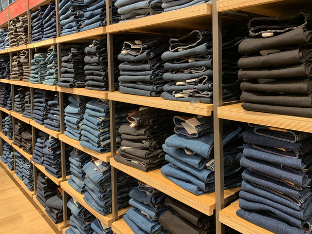 Кучи современных джинсов разных размеров. Выбор джинсов в магазине одежды. Полки с одеждой в отделе хлопка
. - Фото, изображение