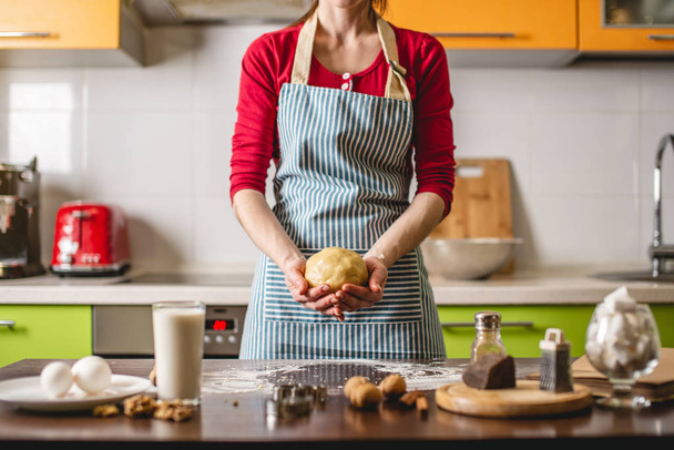 Gotować gospodyni domowa pieczenie ciasteczek w domu na kolorowe kuchnia. Kobieta ugniata dłonie ciasta przy stole ze składnikami - Zdjęcie, obraz