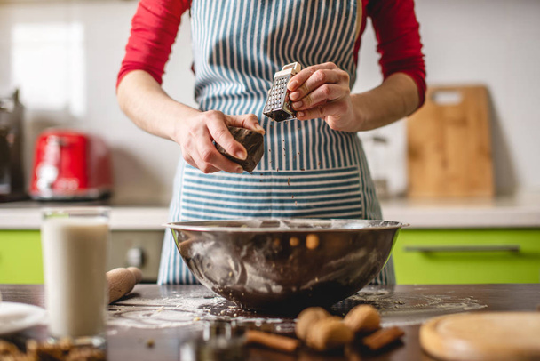 Kokki kotiäiti tekee evästeitä kotona värikkäässä keittiössä. Nainen hankausta raastin suklaa valmistella taikina - Valokuva, kuva