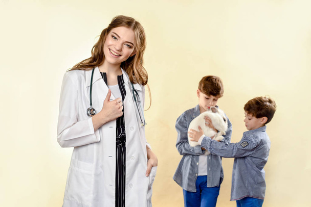Doctor vet doctor examines a pet. Sick rabbit. inoculation to animals. Laughing boy getting back cute pet rabbit from veterinary at pets' clinic. In the studio on a light background - 写真・画像