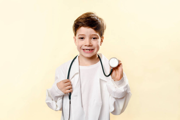 Adorable future doctor a over white background. A boy plays a doctor. children's games. little doctor. white coat and phonendoscope. Emotional baby In a studio - Фото, изображение