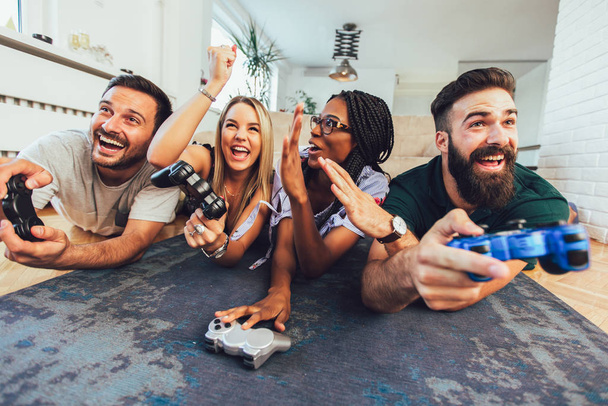 Счастливые мультиэтнические друзья играют в видеоигры и веселятся на ч
 - Фото, изображение