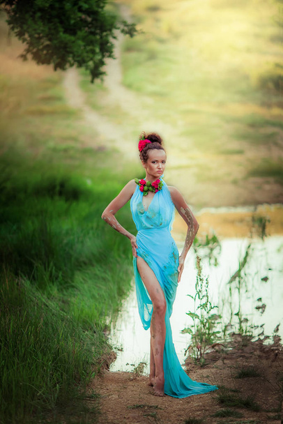 Κορίτσι μοντέλο σε ένα μπλε φόρεμα πλήρους μήκους στο φόντο ενός δασικού δρόμου - Φωτογραφία, εικόνα