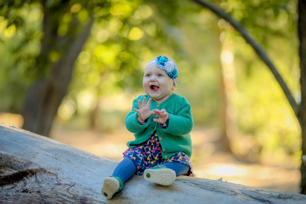 Baby Mädchen sitzt auf einem Baumstamm und lächelt und genießt das Leben - Foto, Bild