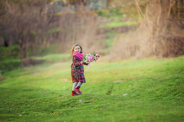 Dziewczyna 7-8 lat w ciepłym płaszczu spaceruje wczesną wiosną na zielonej łące - Zdjęcie, obraz