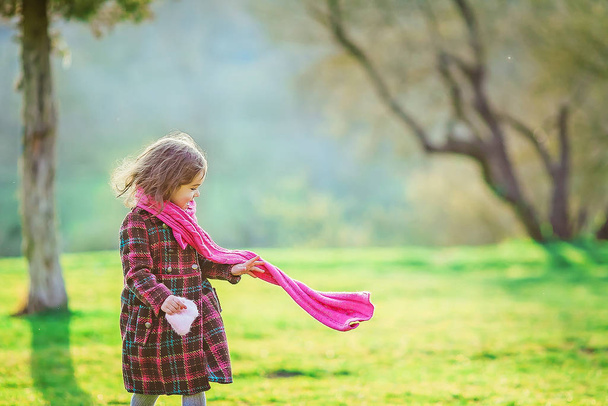 Girl 7-8 years in a warm coat walks in early spring on a green meadow - Foto, Imagen