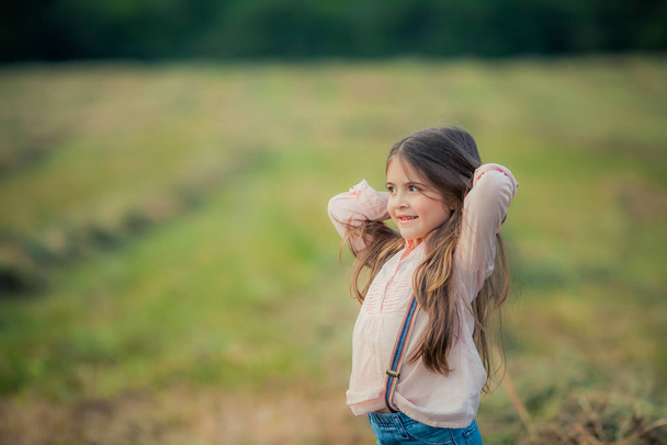 Nahaufnahme eines Kindes in einer rosafarbenen Bluse mit langen dunklen Haaren auf freiem Feld - Foto, Bild